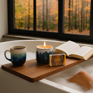 Cup, candle, soap, and book on a bath tray with autumn view outside the window